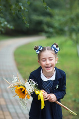 First grader girl with bows and bouquet in the first day of school. the student laughs