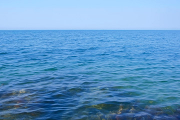 Seascape with transparent blue water, stones and clear sky at sunny day. Nature background with sea water, horizon and sky.