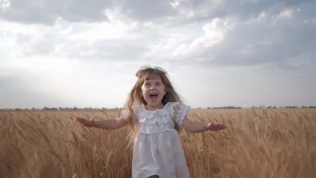 child in field, emotional little girl in white dress runs with arms spread to meeting to across wheat field with golden spikelets of grain in season yield against a blue sky