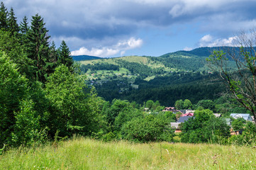 Countryside on the mountainside. The mountains are overgrown with coniferous forest. The blue sky was overshadowed by thunderstorm gray clouds.