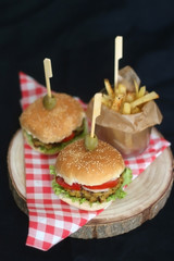 Two homemade vegan burgers made with chickpeas and zucchini, served with salad, tomato, cucumber, pickels and sauce. Fries on the side. Selective focus, dark background.