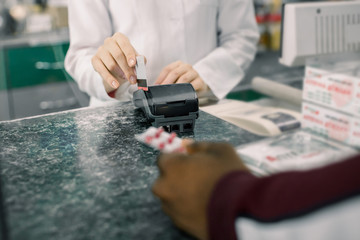 Fototapeta na wymiar Closeup photo of hands of Man paying for Medicaments with credit card in pharmacy drugstore and hands of pharmacist holding terminal.