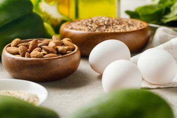 selective focus of nuts in bowls among green vegetables and eggs, ketogenic diet menu