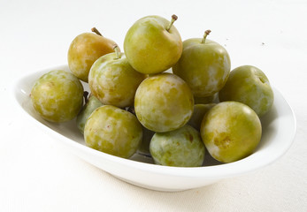 Ciruelas verdes sobre porcelana blanca. Green plums on white porcelain.