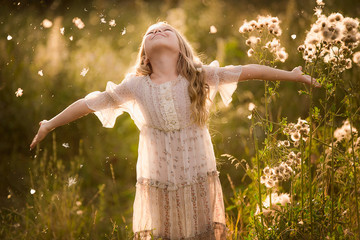 Naklejka na ściany i meble Happy cute girl raises hands on the summer sunshine meadow in front of flying fuzzes