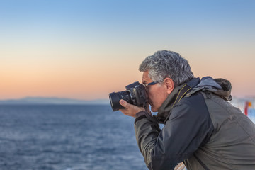 Man taking photographs at sunset from the deck of a ship