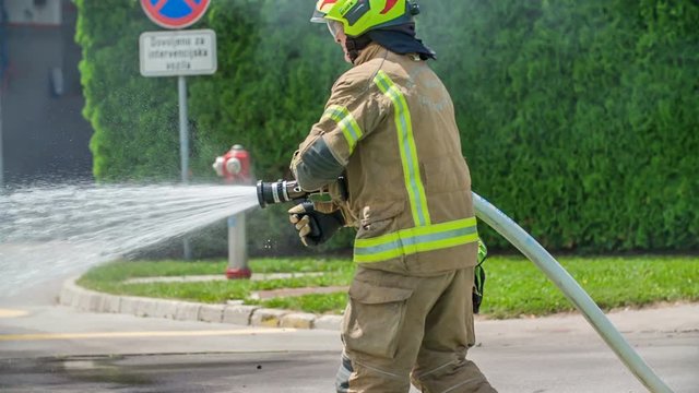 A firefighter is extinguishing a fire and he first needs to open a rubber tube. Firefighter is having a training practise.