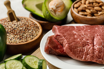 selective focus of raw meat near nuts, groats and green vegetables, ketogenic diet menu