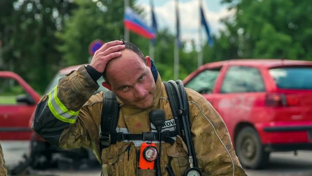 An exhausted firefighter is touching his face and his forehead. He has just finished a firefighting practise.