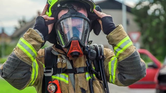 A firefighter is putting on a protection helmet. He also put a mask on his face not to inhale dangerous smoke.