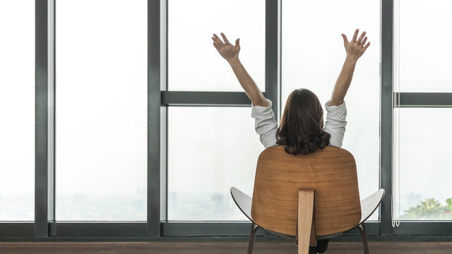 Condo living lifestyle, luxury condominium home life style of happy working woman take it easy relaxing, resting on comfort chair in building tower or city hotel lobby interior with rooftop view