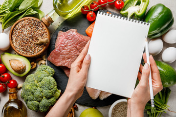 cropped view of woman holding empty notebook above food for ketogenic diet menu - obrazy, fototapety, plakaty
