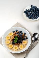 Oatmeal porridge with bananas, walnuts, blackberries, blueberries, honey and mint in a white bowl on a white background. Healthy breakfast and homemade diet food.
