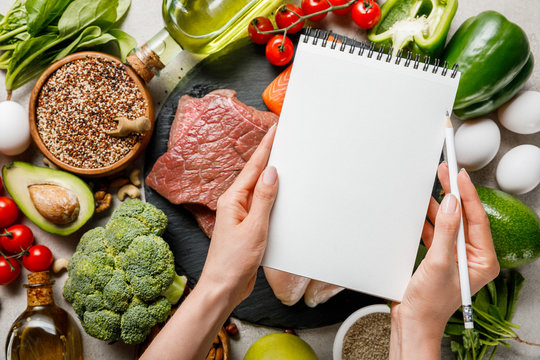 cropped view of woman holding empty notebook above food for ketogenic diet menu