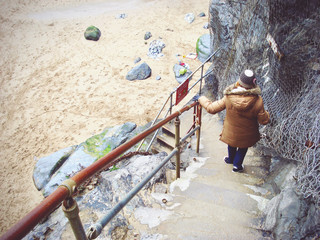 Young woman in winter puff jacket and woolen hat holding the fence and descending concrete stairs...