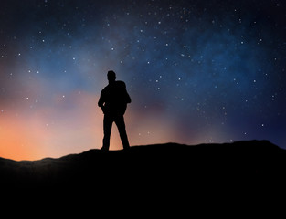 travel, tourism, hike and people concept - silhouette of traveler standing on edge of mountain over starry night sky or space background