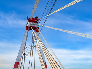 Cable-stayed bridge with high red and white tower and steel cables against blue sky.