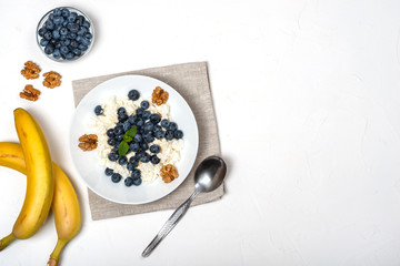 Healthy breakfast. Cottage cheese with blueberry, nuts, honey and mint in a white bowl on a white background. Top view. Copy Space.