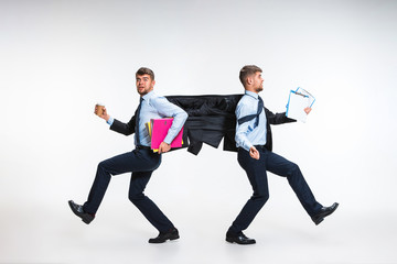 Young man torning between cases and trying to do everything - holding folders and documents on the run in different directions. Concept of office worker's troubles, business, problems, stress.