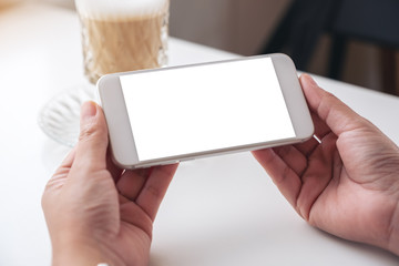 Obraz premium Mockup image of a woman holding white mobile phone with blank desktop screen with a glass of coffee on the table