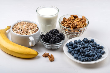 Ingredients for the healthy breakfast. Oatmeal, milk, blackberry, blueberry, bananas, walnuts on the white background