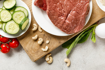 fresh raw meat on white plate near nuts and cucumbers, ketogenic diet menu