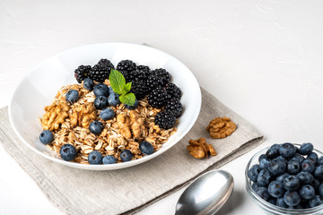 Healthy breakfast. Homemade granola, muesli, cereals with blackberries, blueberries, nuts, honey and mint in a white bowl on a white background.