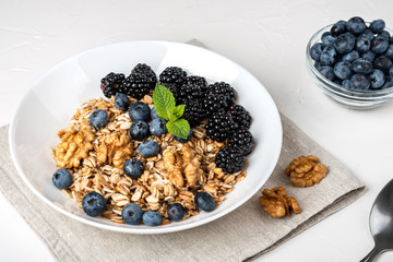 Healthy breakfast. Homemade granola, muesli, cereals with blackberries, blueberries, nuts, honey and mint in a white bowl on a white background.
