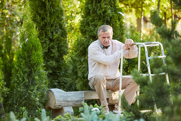 Full length portrait of lonely senior man with walker sitting on park bench outdoors, copy space