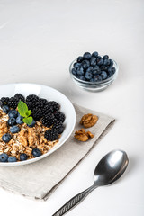 Healthy breakfast. Homemade granola, muesli, cereals with blackberries, blueberries, nuts, honey and mint in a white bowl on a white background.