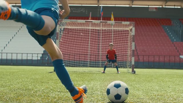 Small goalie waiting on his post while opposite player taking a run and kicking ball, but shooting wide