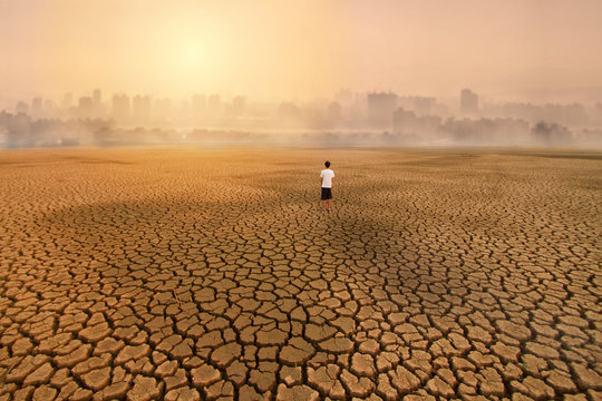 a man standing at empty land of dry cracked earth and looking to the big city with air polluted environment metaphor Climate change, Water crisis, Environment pollution of activity from urban concept.