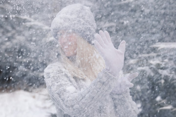 Young beautiful girl with long white hair plays snowballs. She has fun, throws snow and rejoices the snowfall. Winter walk outside.