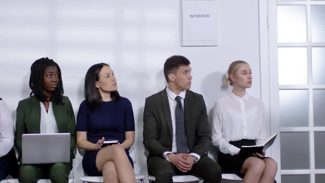 PAN shot of male HR manager in suit walking into office reception are and calling man in formalwear in for job interview while other candidates waiting for their turn
