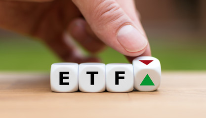 Hand is turning a dice and changes the direction of an arrow symbolizing that the value of an ETF...