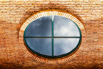 Round old glass window on the orange bricks wall at the facade of the building