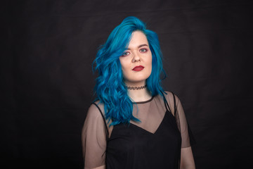 people, fashion and hair concept - close-up portrait of young woman in black dress with blue hair on black background