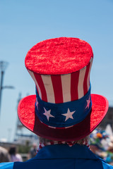 Unidentifiable person wearing American Flag red white and blue top hat. There is a blue sky in the...