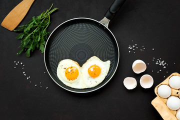 Fried eggs in frying pan with arugula leaves, salt and pepper for breakfast on black wooden background. Top view. Flat lay. Copy space. Healthy food concept