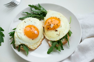 Sandwiches with ricotta cheese, arugula and fried egg on white wooden background. Selective focus. Healthy food concept