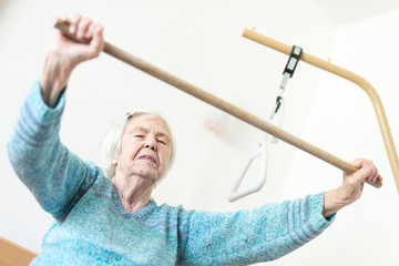 Elderly 96 years old woman exercising with a stick sitting on her bad. Geriatric health care home...