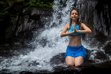 Young Caucasian woman meditating, practicing yoga at waterfall in Ubud, Bali, Indonesia. Close up.