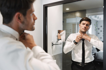 Image closeup of handsome man wearing formal suit looking at mirror in bathroom at hotel room...
