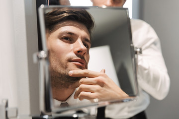 Image closeup of handsome man looking at mirror in bathroom at hotel room during business trip