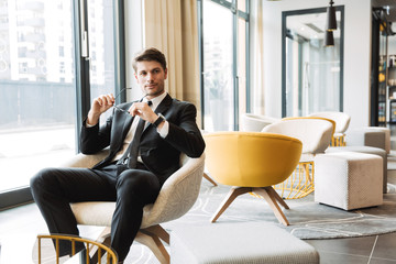 Photo of confident young man holding eyeglasses in hotel hall during business trip