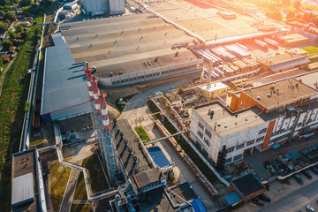 Aerial view of industrial area with warehouses, factory buildings and chimney on foreground at sunset, drone photo