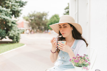 Summer. Beautiful young woman sitting in a street cafe and tastes ice cream. Copy space