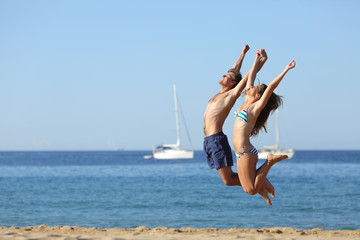 Excited couple jumping on the beach celebrating vacation