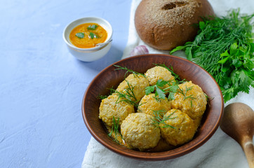 Delicious dinner: meatballs from minced meat with greens sauce and fragrant bread in a clay plate and with a wooden spoon on a blue background for the menu