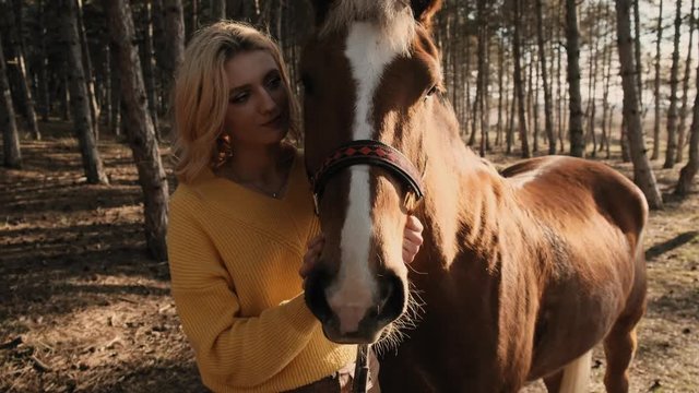 Beautiful blone woman is enjoing the hugging of sweet handsome horse in the wood close up slow motion